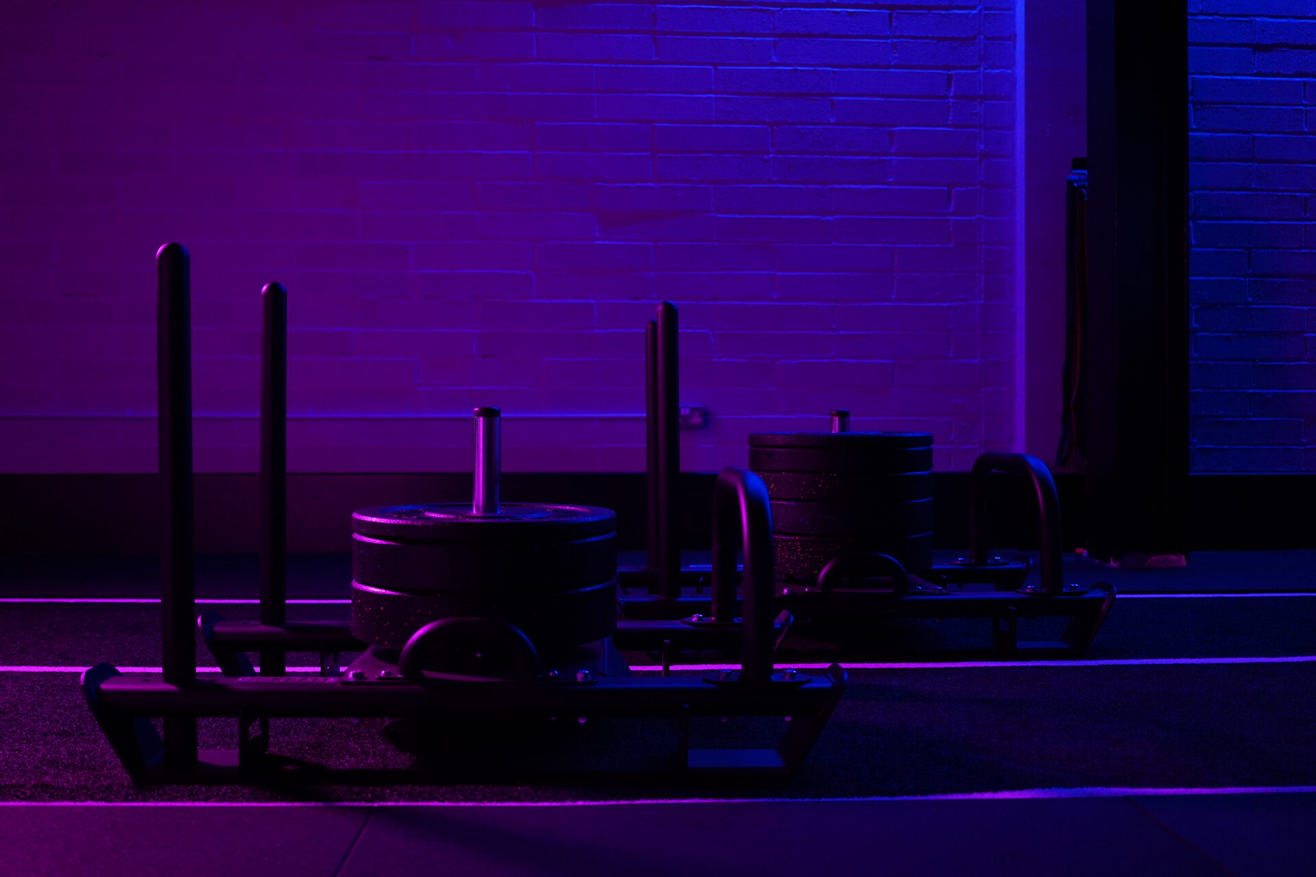 Prowler push sleds loaded with plates on the turf sprint lane at CXHW's Hackbridge studio, lit in purple